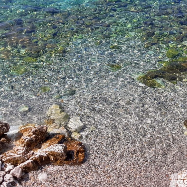 Klares, türkisfarbenes Wasser über Kies- und Steingrund, mit glitzerndem Lichtspiel.