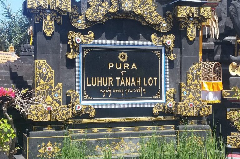 Schwarzer Steinsäulen mit goldenen Verzierungen und der Inschrift "Pura Luhur Tanah Lot".