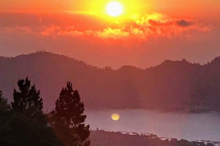 Sonnenuntergang über Bergen mit reflektierendem Licht auf dem Wasser.