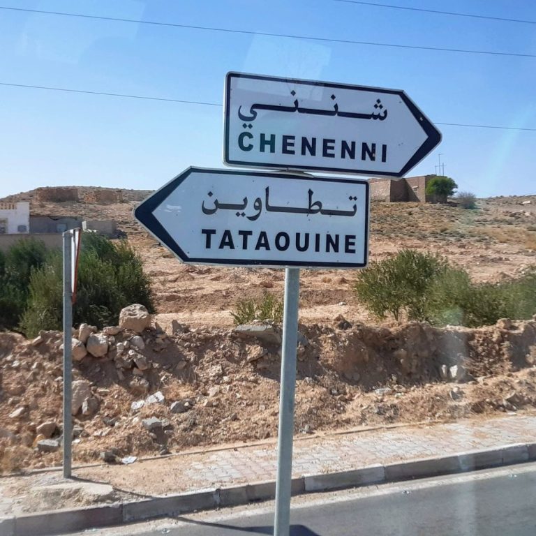 Wegweiser zu den Städten Cheninni und Tataouine in einer trockenen, landschaftlichen Umgebung.